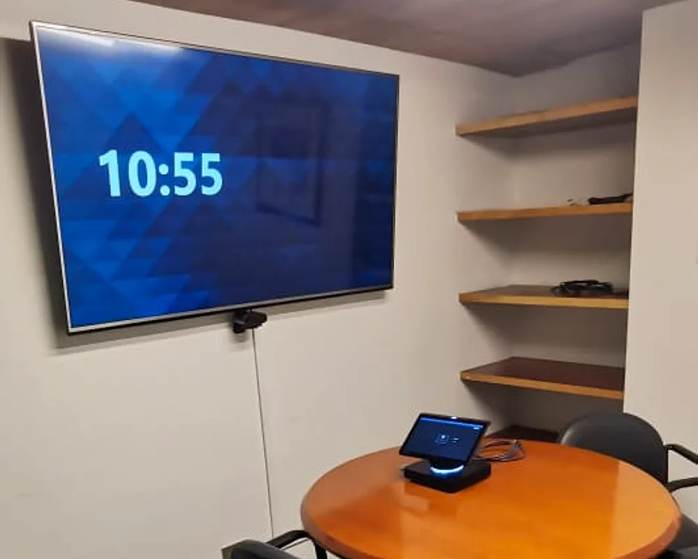 Sala de reuniones pequeña con mesa redonda y pantalla con barra de video