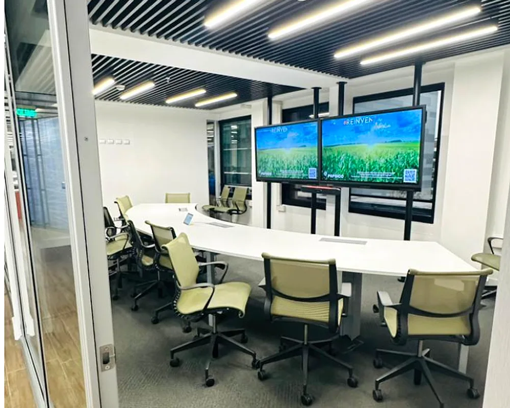 Sala de reuniones grande con mesa larga, doble pantalla y barra de video