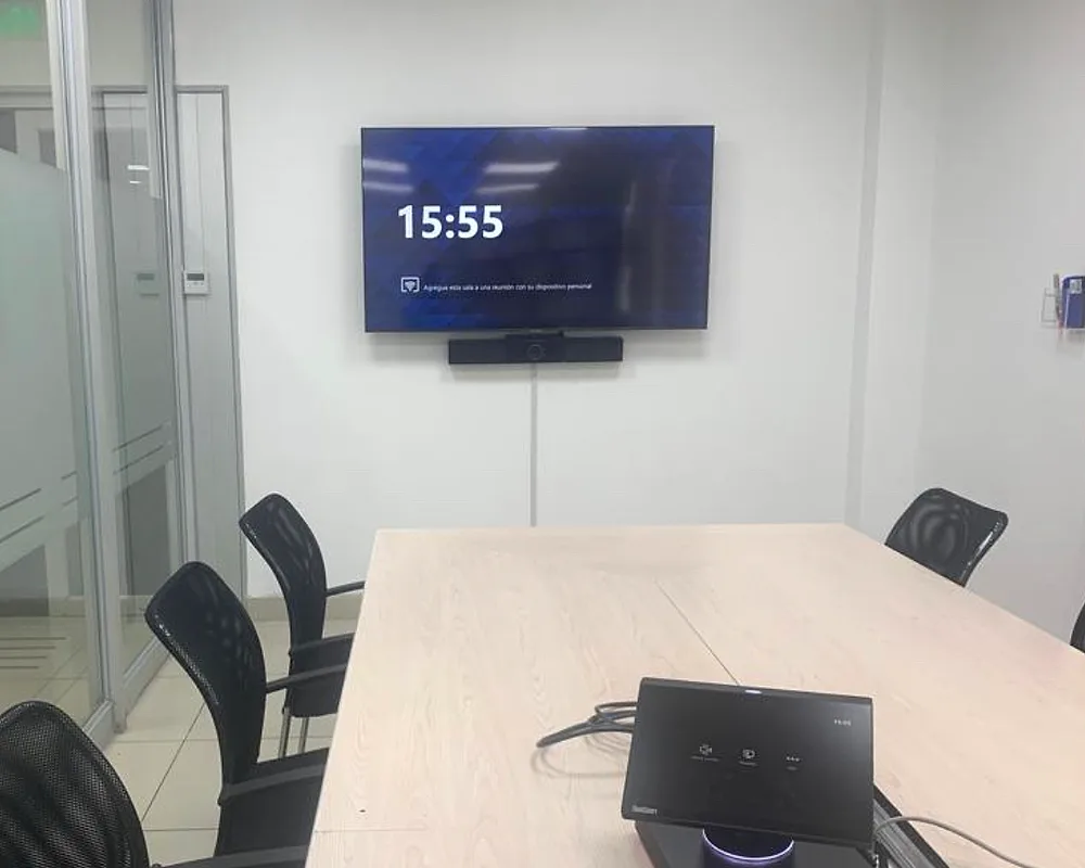 Sala de reuniones mediana con pantalla en la pared y equipo de videoconferencia